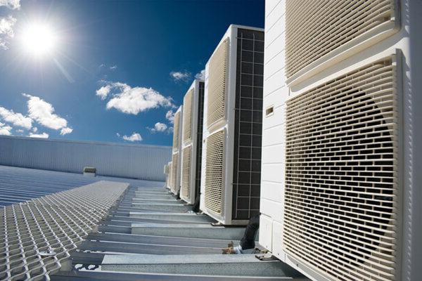 White air conditioner units on a roof of industrial building with blue sky and clouds in the background