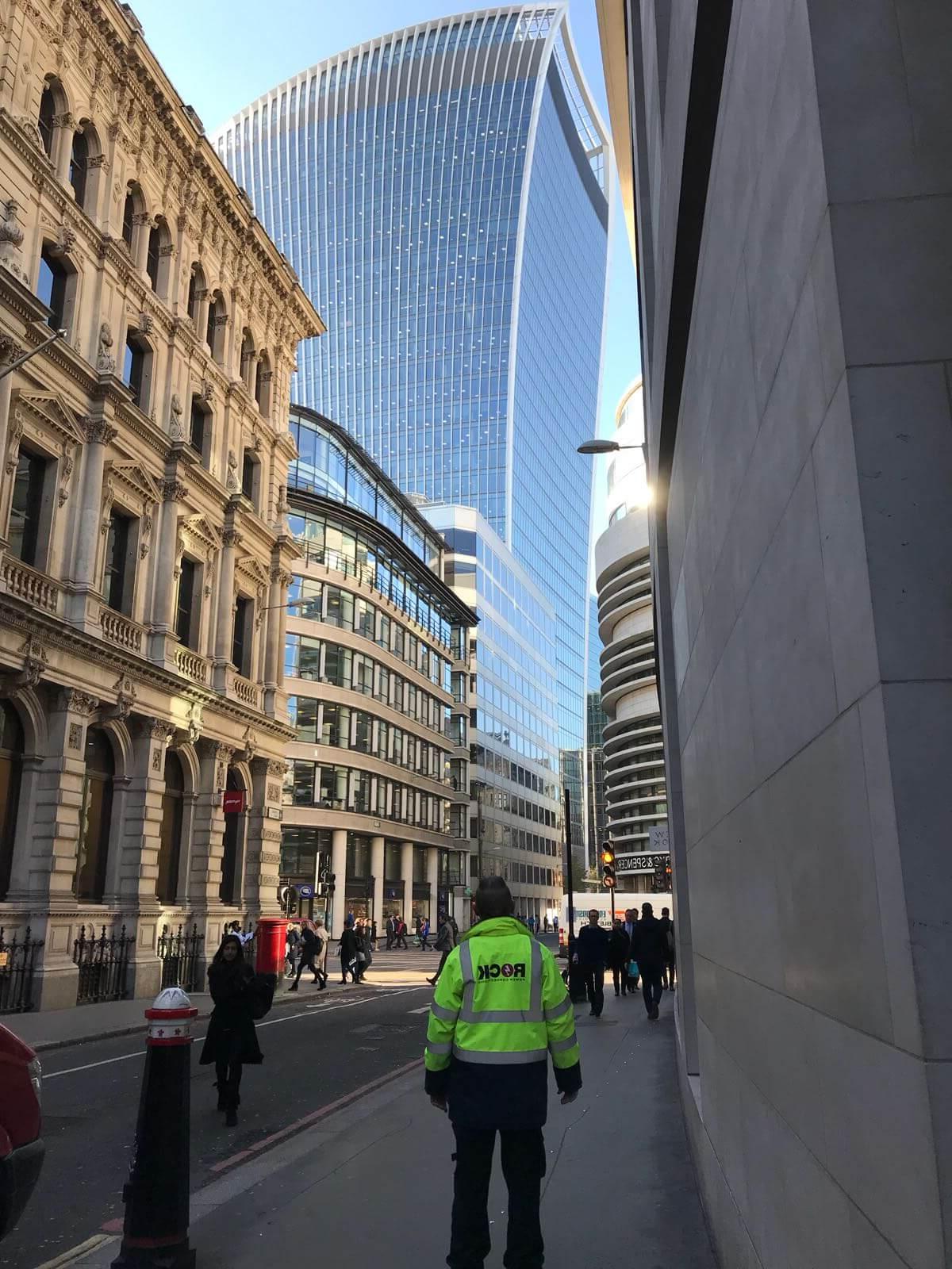 A Rock Power Connections employee in a hi vis jacket, looking up at a London skyscraper building