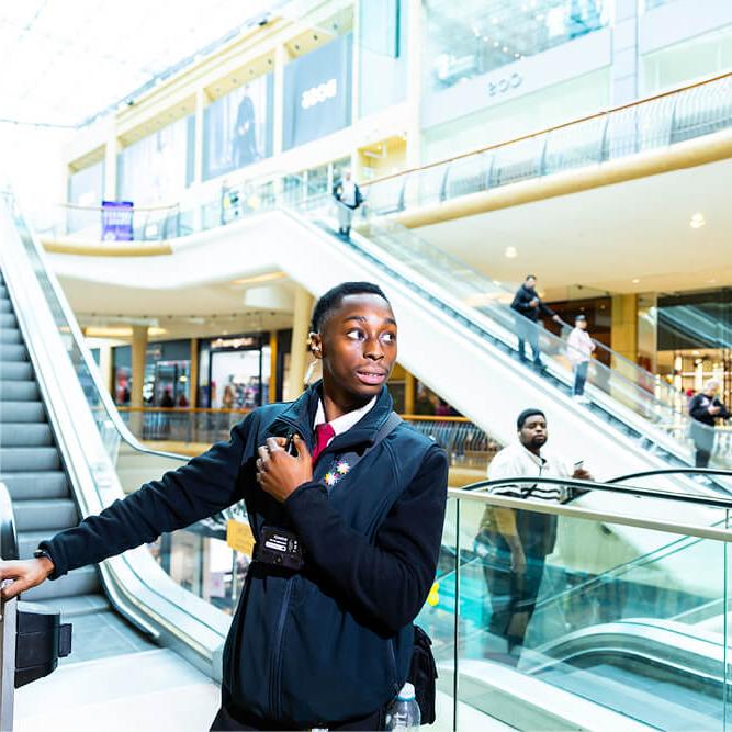 A black male security guard standing at the bottom of an escalator in a shopping centre