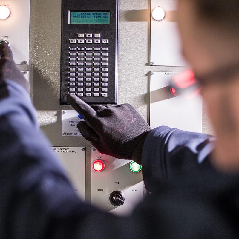 Close up of a Mitie engineer wearing black gloves pressing buttons on a control panel