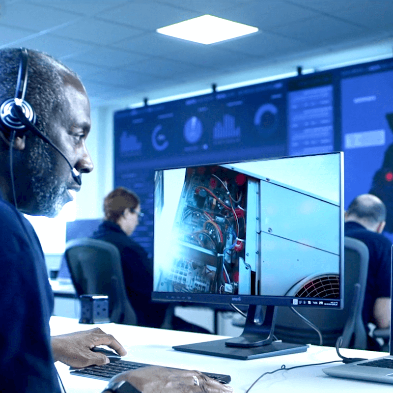A remote maintenance worker at Mitie's Technical Services Operations Centre. Wearing a headset and looking at a monitor, seeing what an engineer is seeing on site